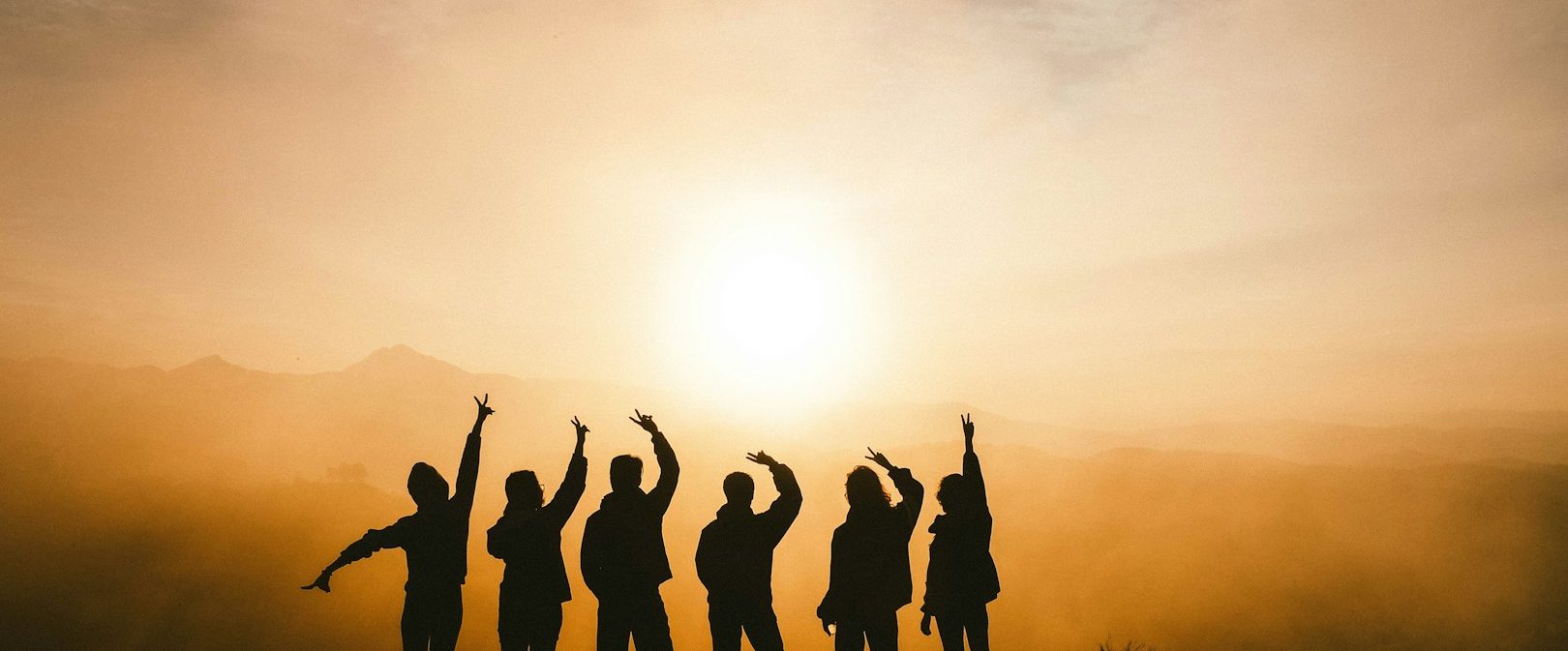 Gemeinschaft Silhouette von sechs Personen, die vor einem Sonnenuntergang jubeln.