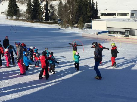 Rossi cLUB Kinder in Winterkleidung üben Skifahren auf einer verschneiten Piste.